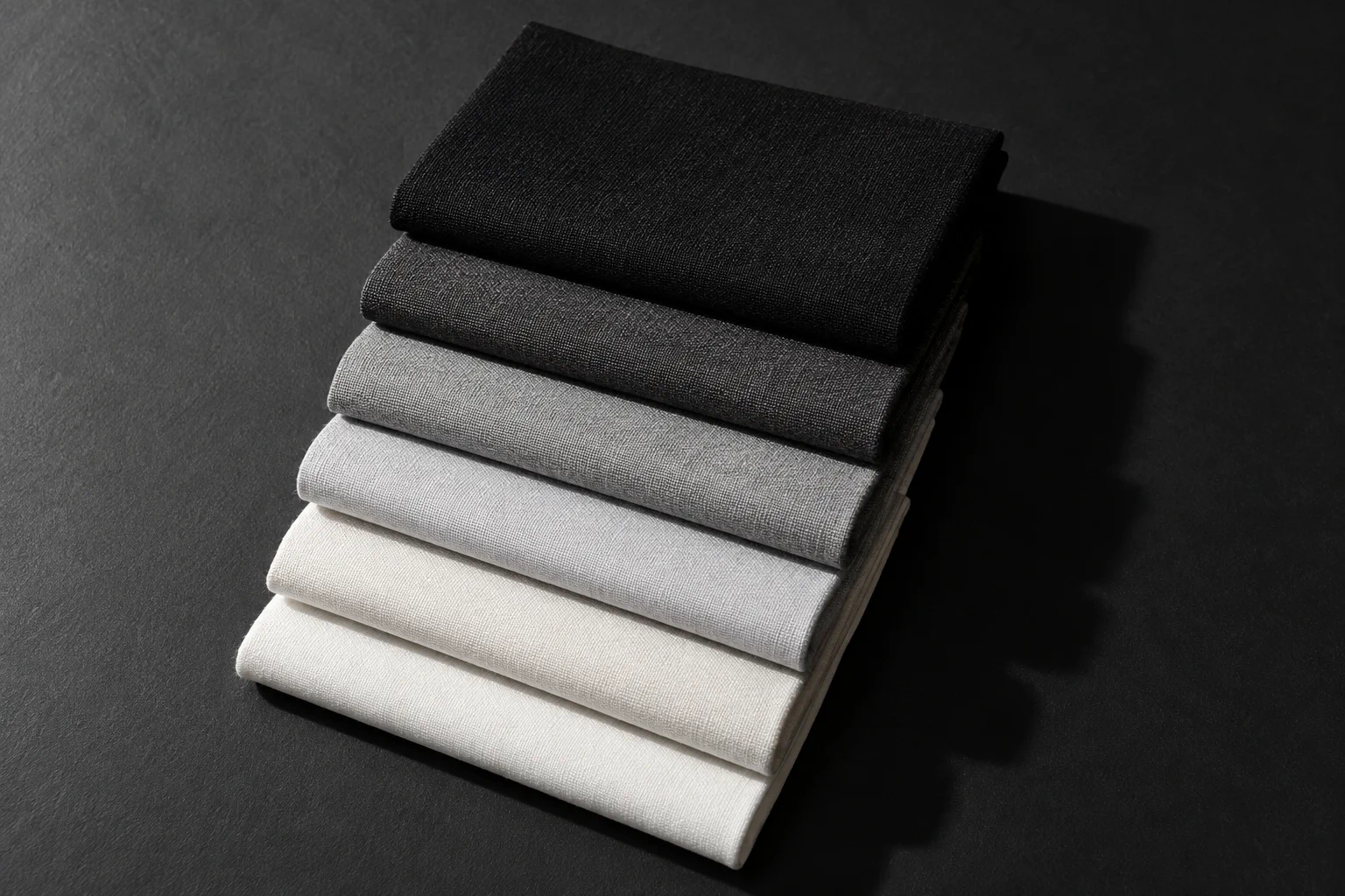 Sechs gefaltete Stoffmuster, von Schwarz bis Off-White.